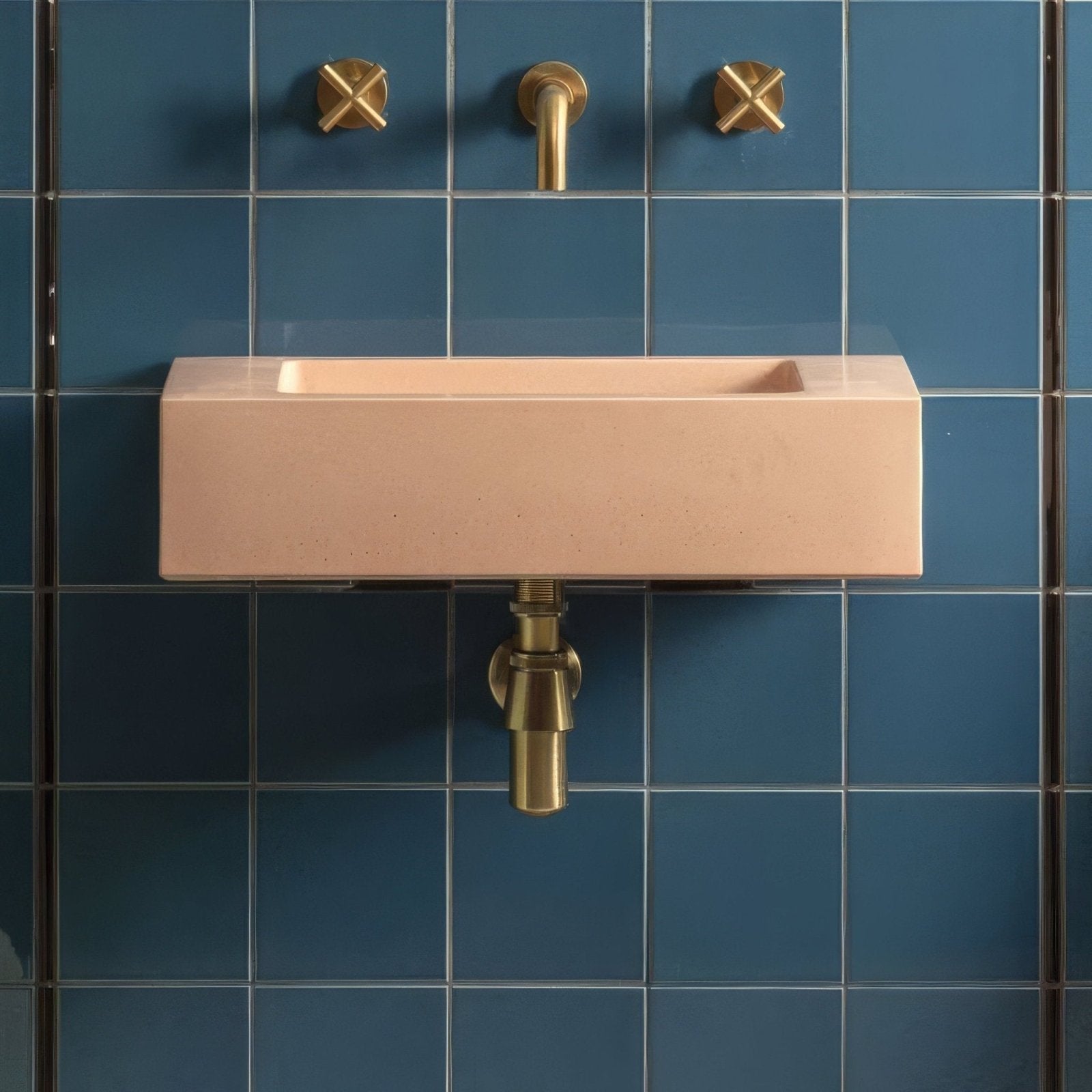 A sleek peach-colored concrete rectangular sink with brass fixtures mounted on baroque blue field tile walls