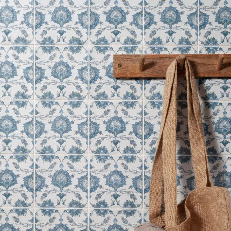 A beige jute tote bag hangs from a wooden hook against a wall of blue and white patterned tiles.