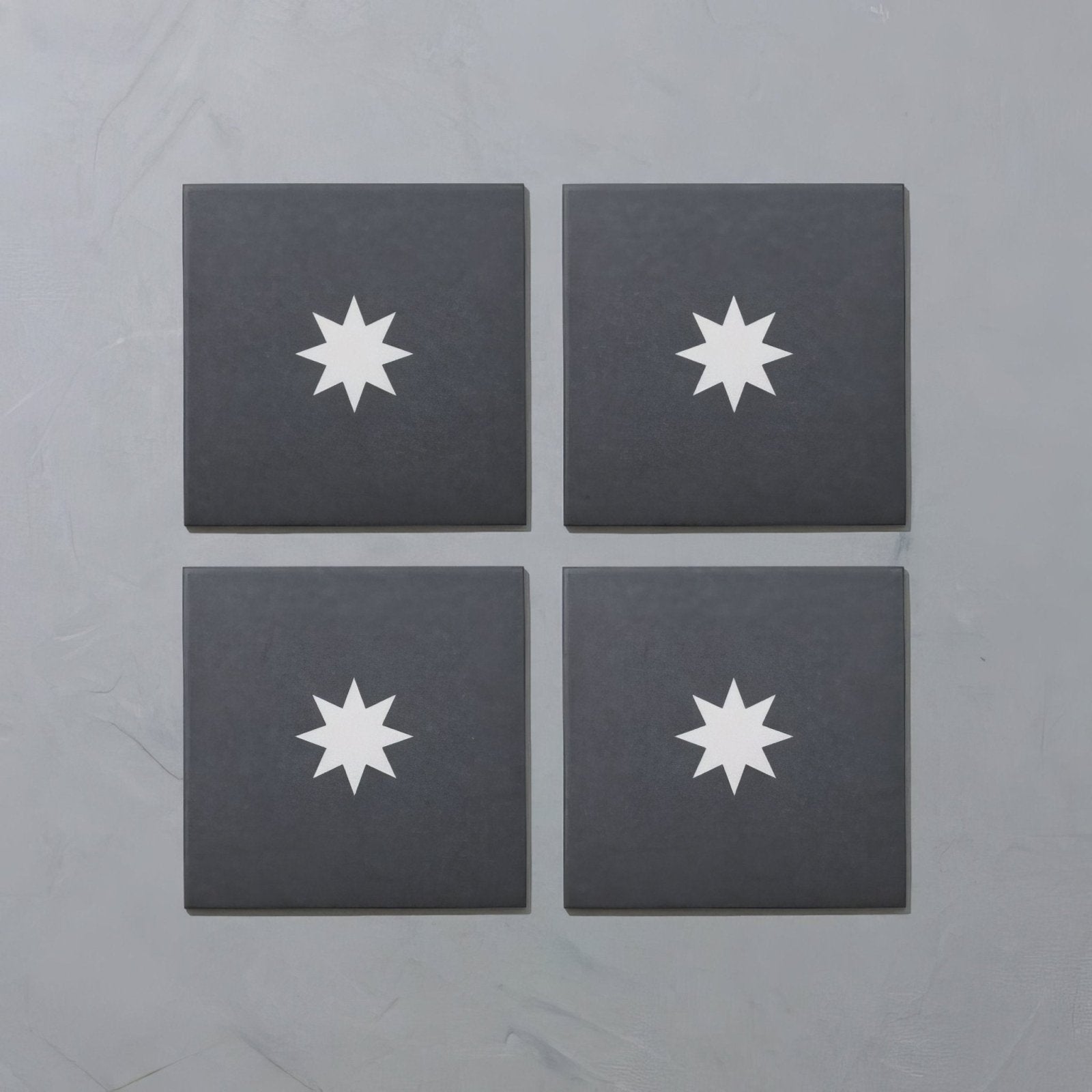Set of four dark gray porcelain square coasters by Bert & May featuring a white starburst design