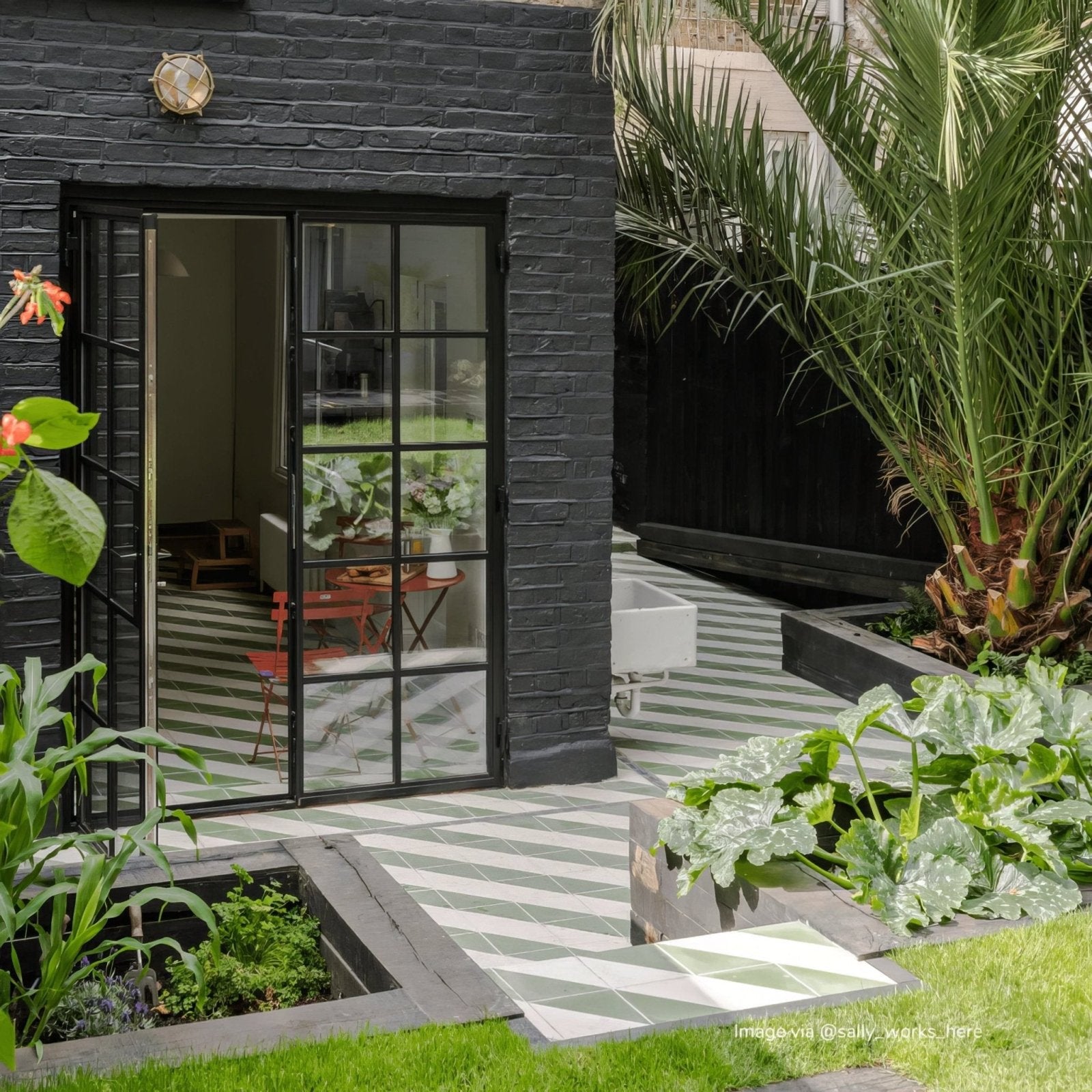 Black brick exterior wall with bert and may green alalpardo porcelain glass door surrounded by greenery