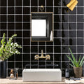 White rectangular ceramic sink with brushed brass faucet and matching wall-mounted mirror above black field tile wall