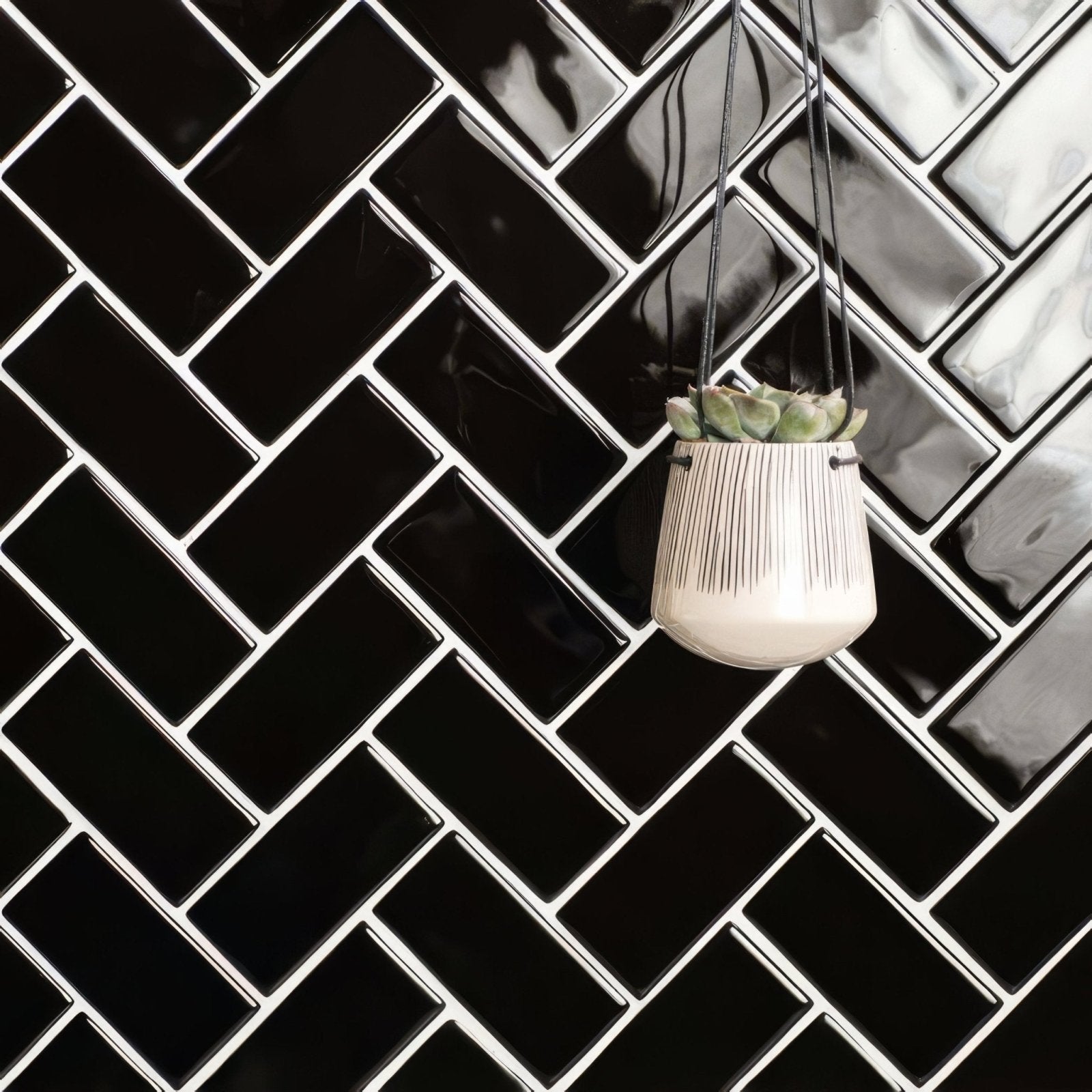 Black half tile cream-colored ceramic hanging planter with vertical black stripes holding a small succulent