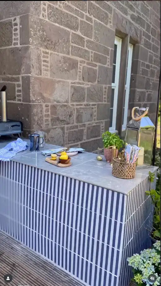 Blue and white striped tiled outdoor kitchen counter beside a stone wall.