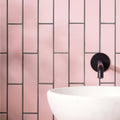 A sleek matte black wall-mounted faucet with minimalist design shown against blush smooth brick tile background