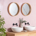 Two round mirrors with light wood frames mounted above white ceramic vessel sinks on blush smooth brick tile wall