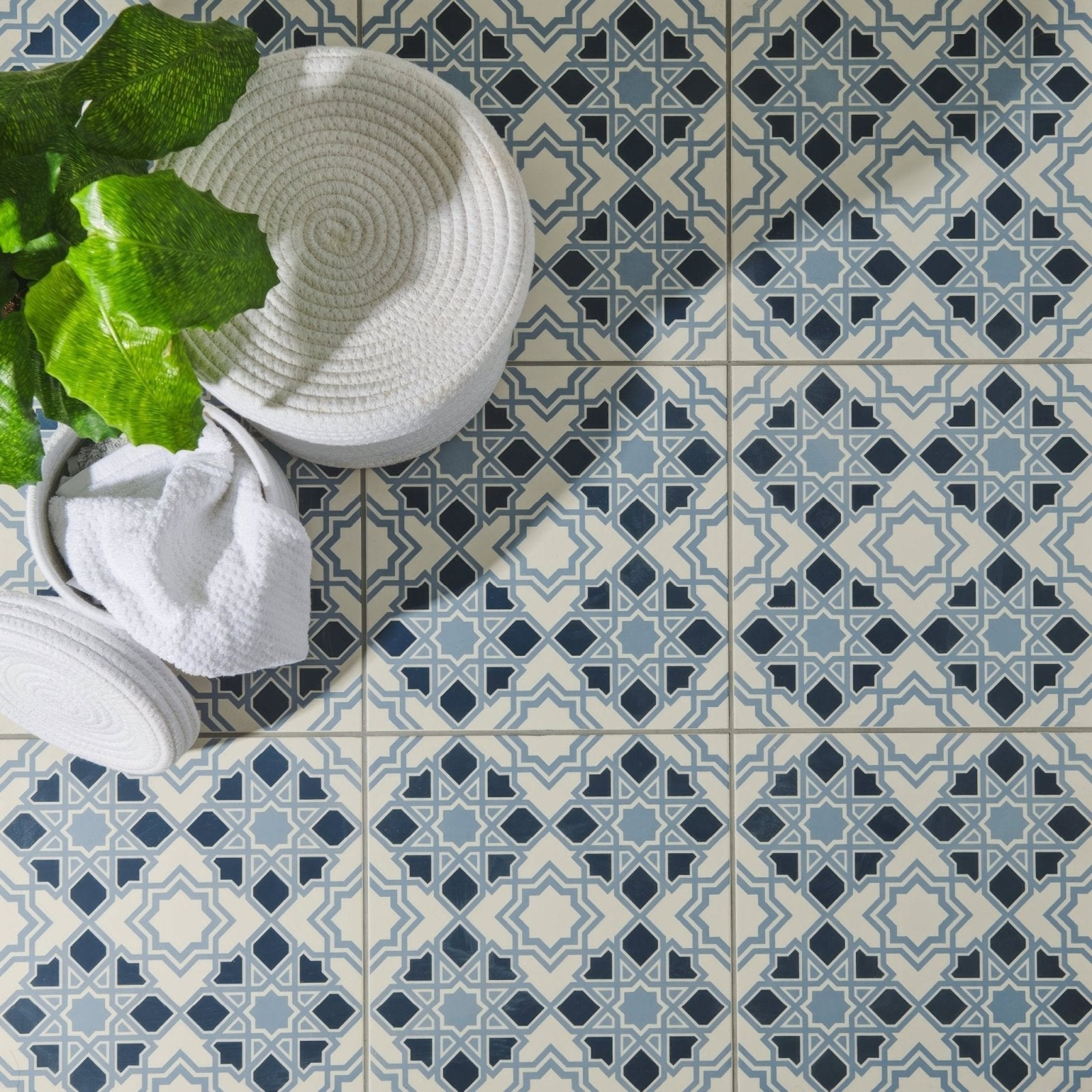 Bolero light dark blue geometric patterned floor tiles with cream accents beside a woven white basket and green plant