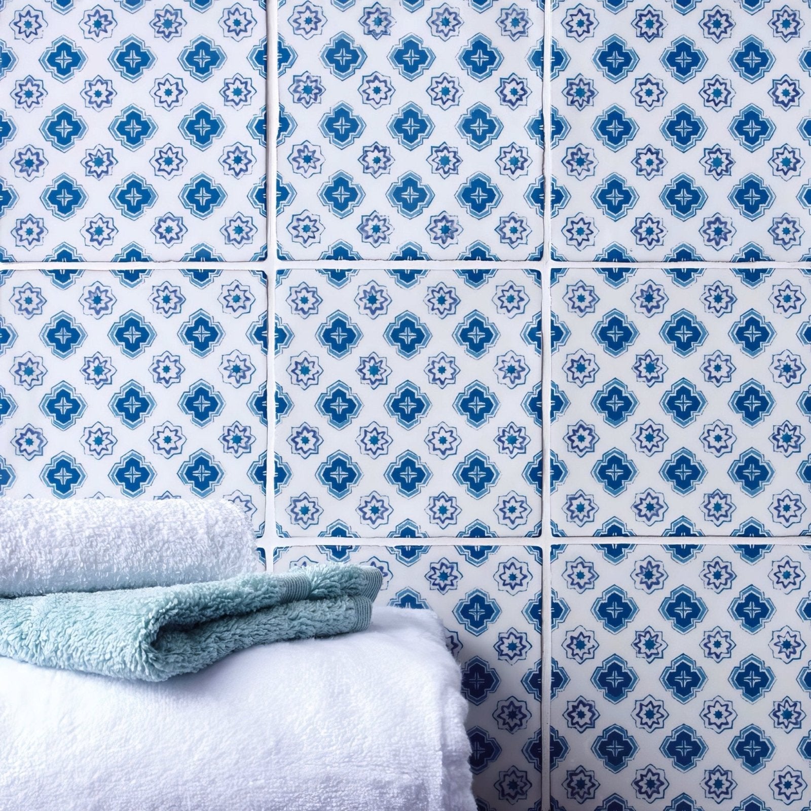 Stack of plush white and light blue towels against patterned blue and white ceramic tiles in bourron on papyrus