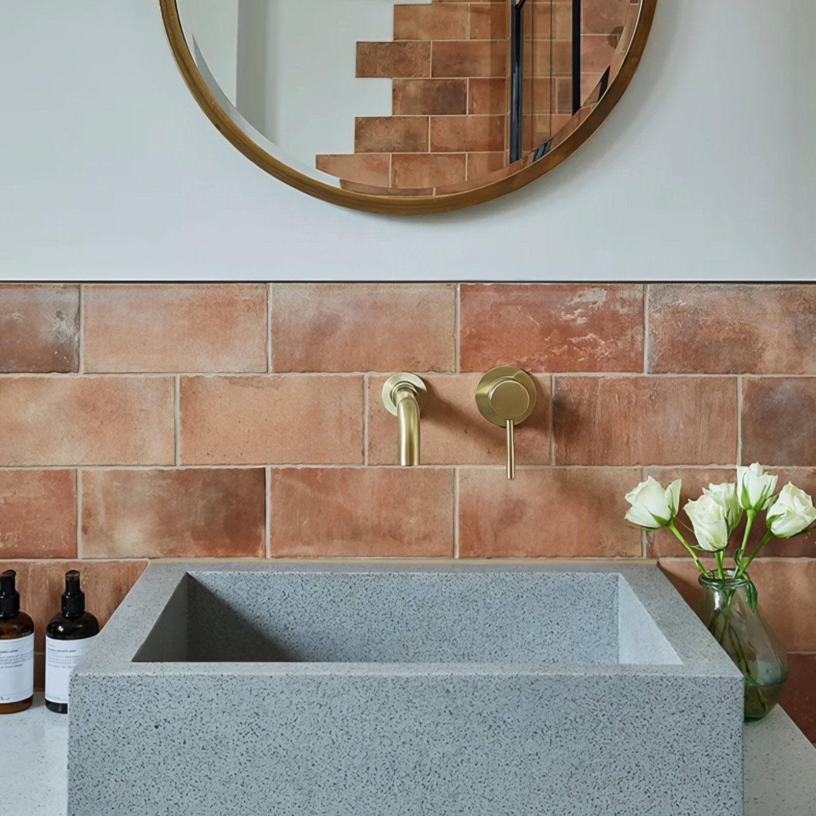 Gray speckled stone rectangular brewhouse porcelain brick sink with modern brass faucet against terracotta tiled wall