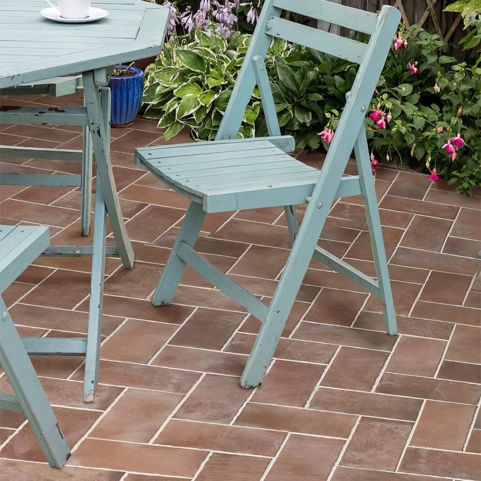 A light blue wooden folding chair with a slatted seat and backrest showing wear edges brewhouse porcelain brick