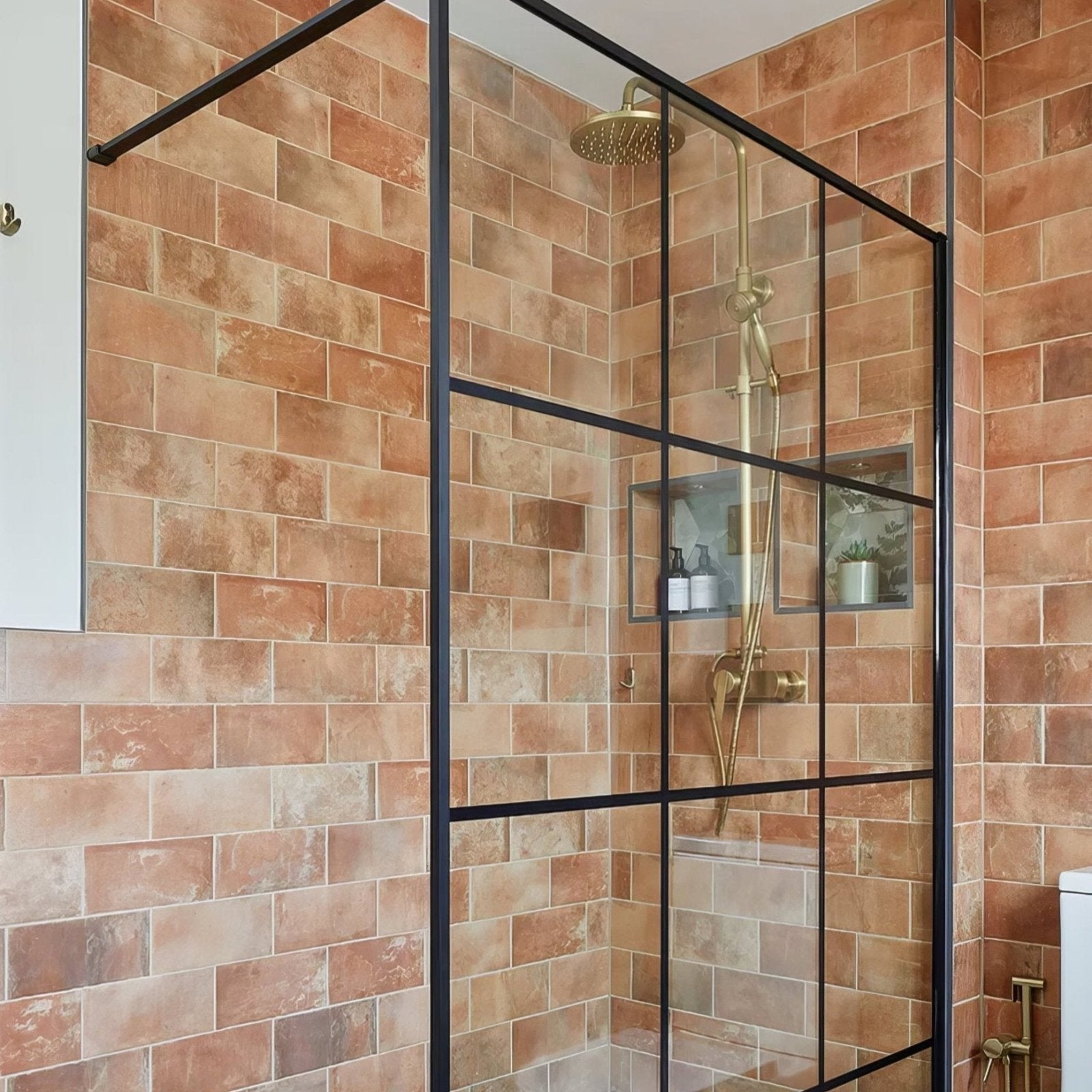 Modern black-framed glass shower enclosure with gold-toned rainfall showerhead in brewhouse porcelain brick setting