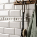Black wooden-handled bath brush with natural bristles hanging from rope for use with brilliant white dentil moulding