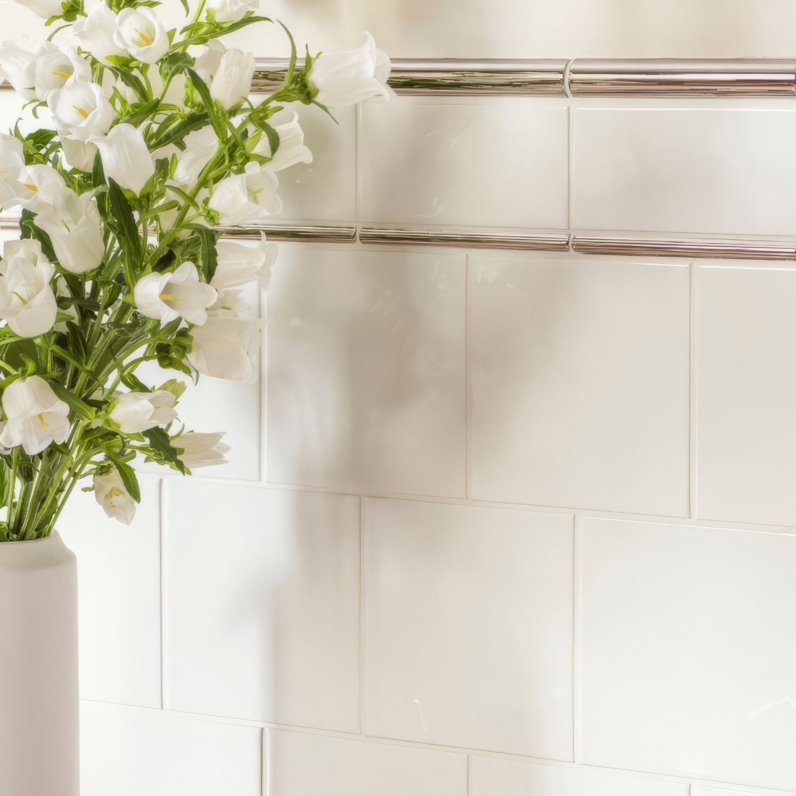 A sleek white ceramic vase with fresh white bellflowers displayed on brilliant white field tile