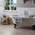 White clawfoot bathtub with black feet and silver faucet against brilliant white half tile wall background