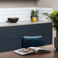 A dark teal quilted leather chair with diamond-stitched pattern next to brilliant white metro bevelled tile wall