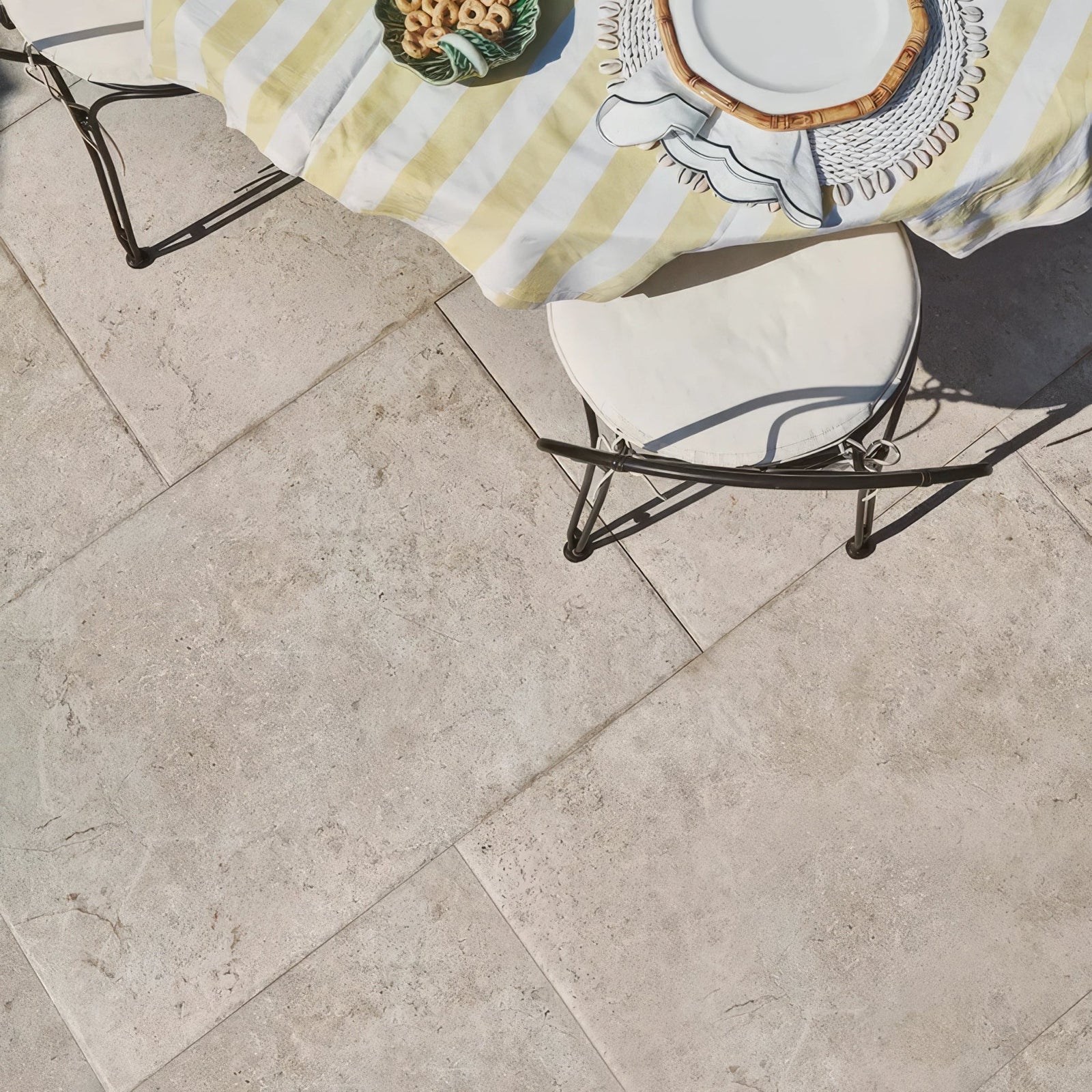 A white cushioned chair with black metal legs on a light beige brit stone burford porcelain paving patio