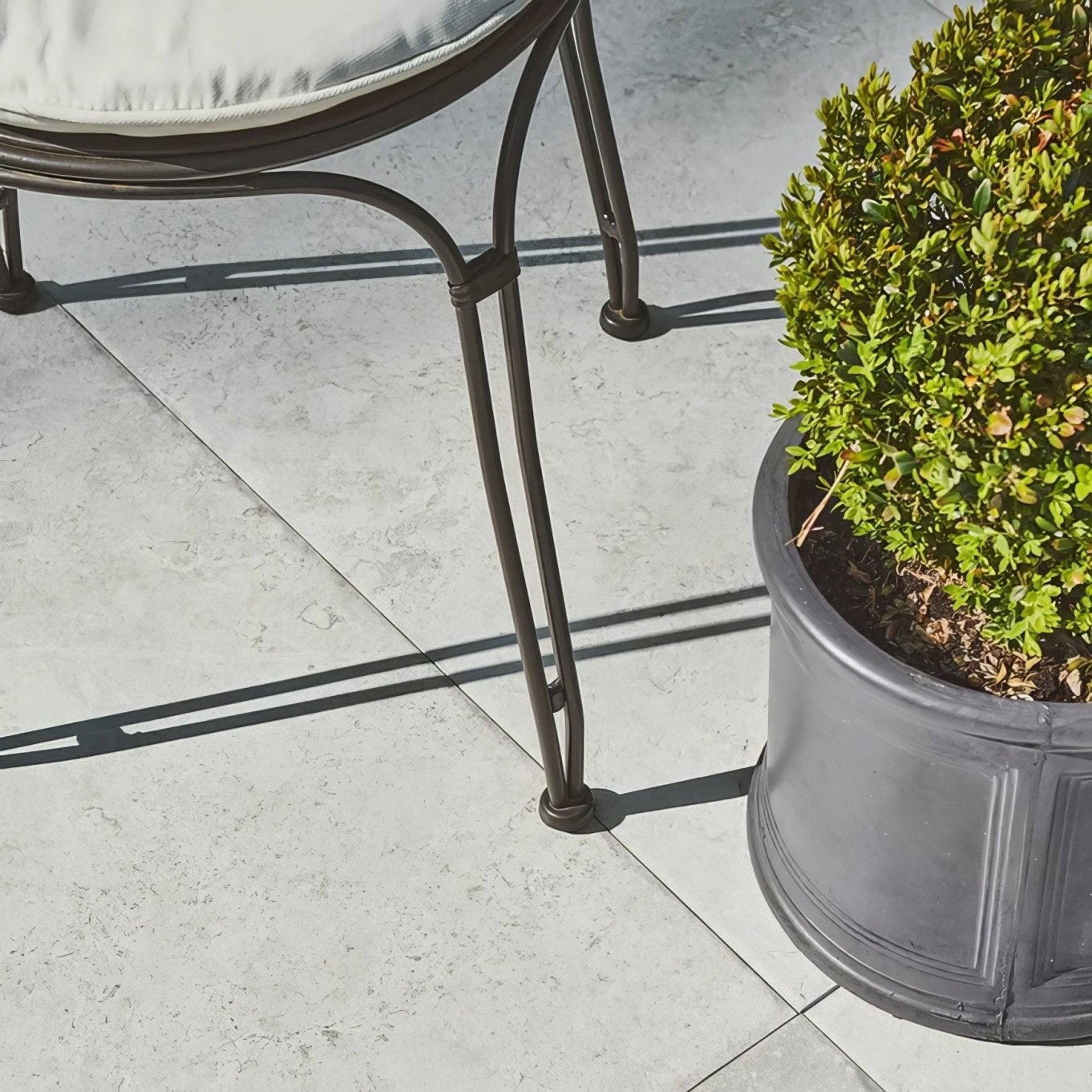 Dark metal patio chair with curved legs and light cushion on brit stone minster porcelain paving outdoors