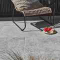Woven rattan lounge chair with black metal frame and beige textured cushion on brit stone pennant porcelain paving