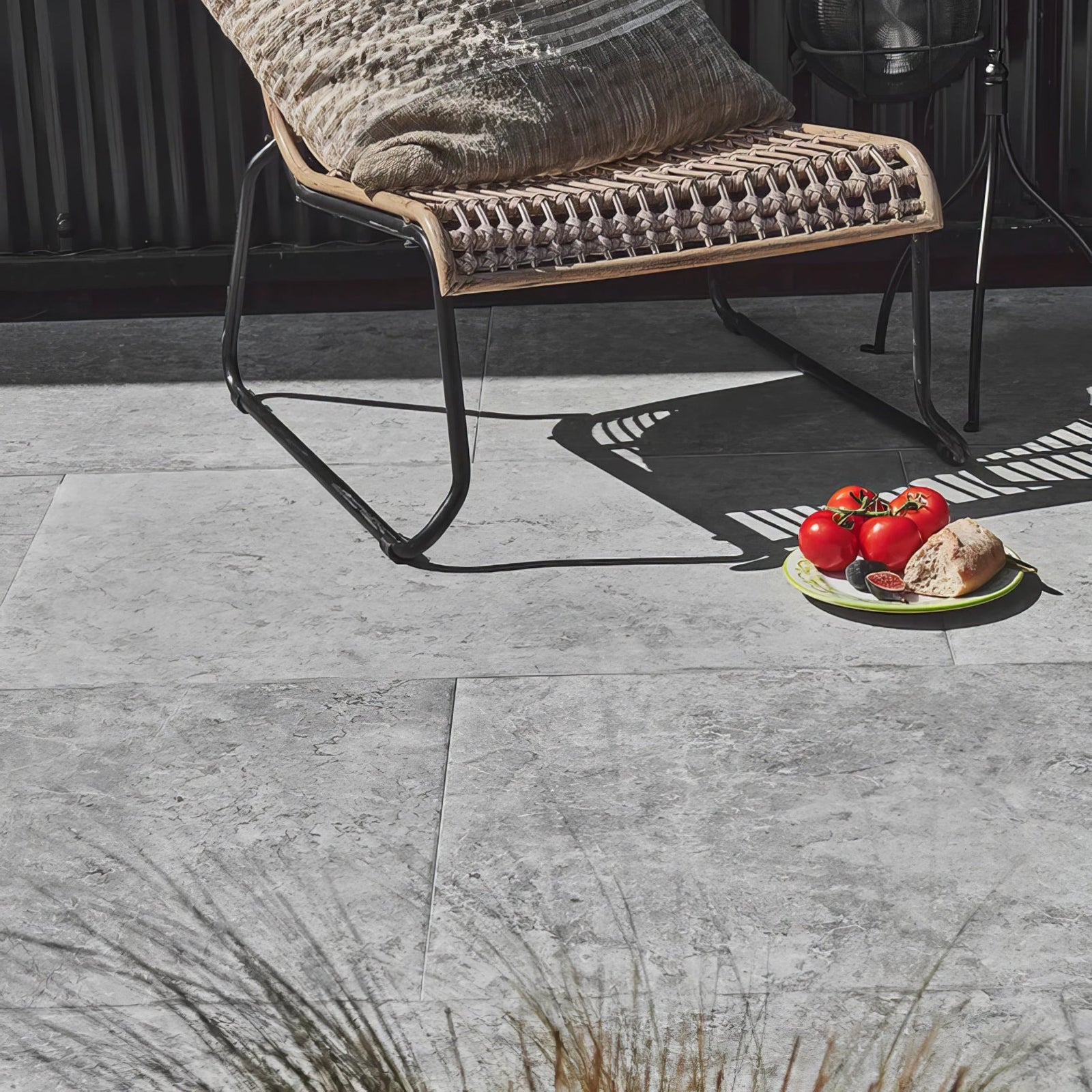 Woven rattan lounge chair with black metal frame and beige textured cushion on brit stone pennant porcelain paving
