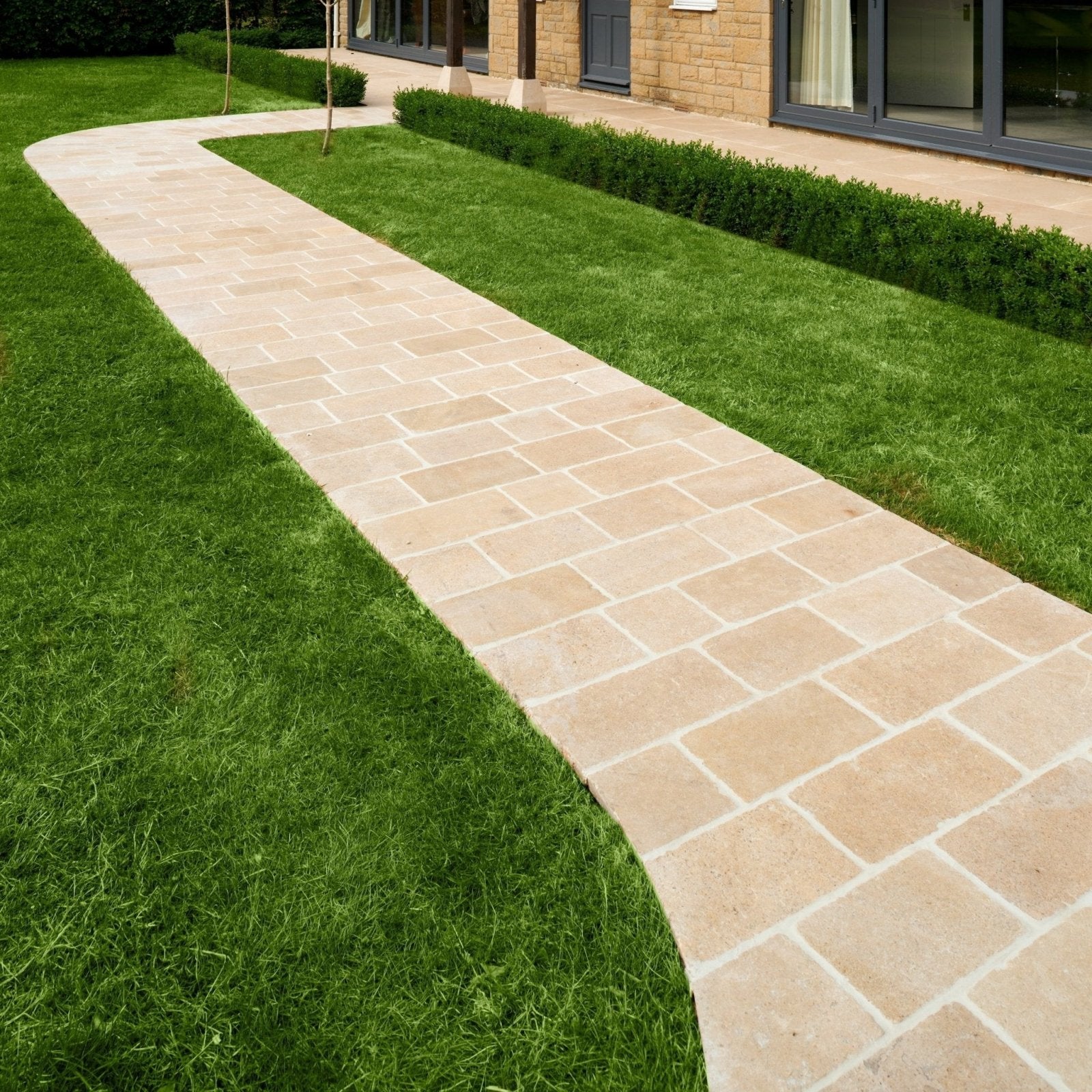 Beige buscot limestone cobble pathway with tumbled and etched finish rectangular pavers and light gray grout bordered by grass