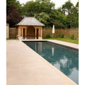 Buscot limestone etched bullnose coping in light beige stone tiles surrounding a rectangular pool with clear blue water