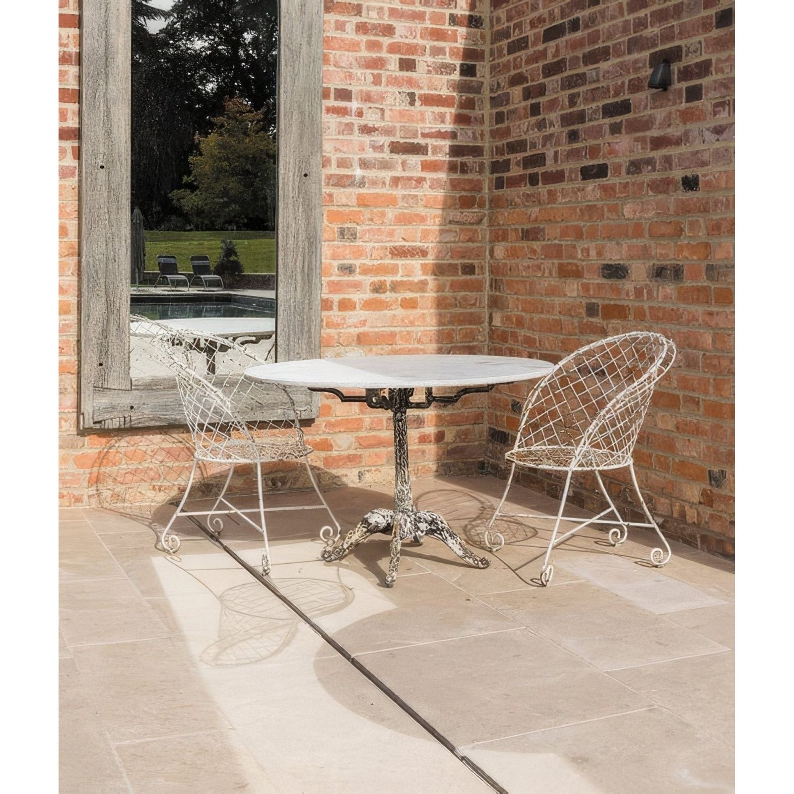 White wrought iron table with marble top and ornate scrolled legs featured with buscot limestone paving tumbled and etched finish