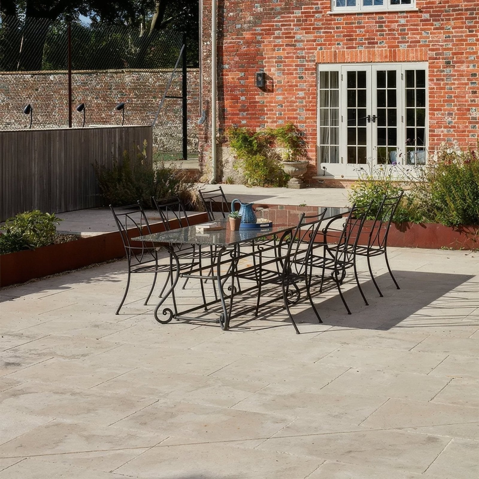 Black wrought iron garden dining set with glass table and ornate scrollwork legs from buscot limestone tumbled finish
