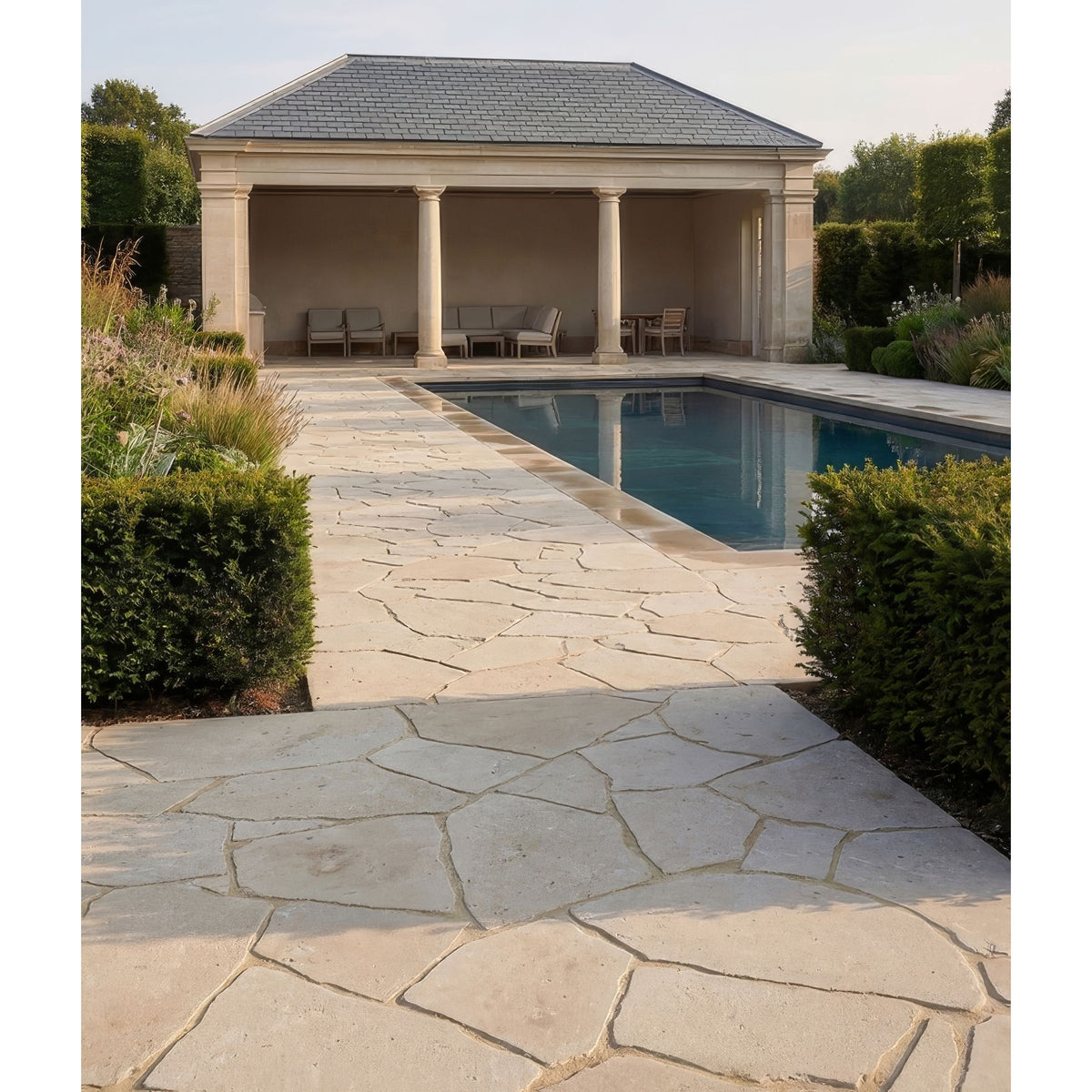 Beige buscot limestone tumbled pietra pazza stone pathway with irregular natural slabs leading to a poolside pavilion