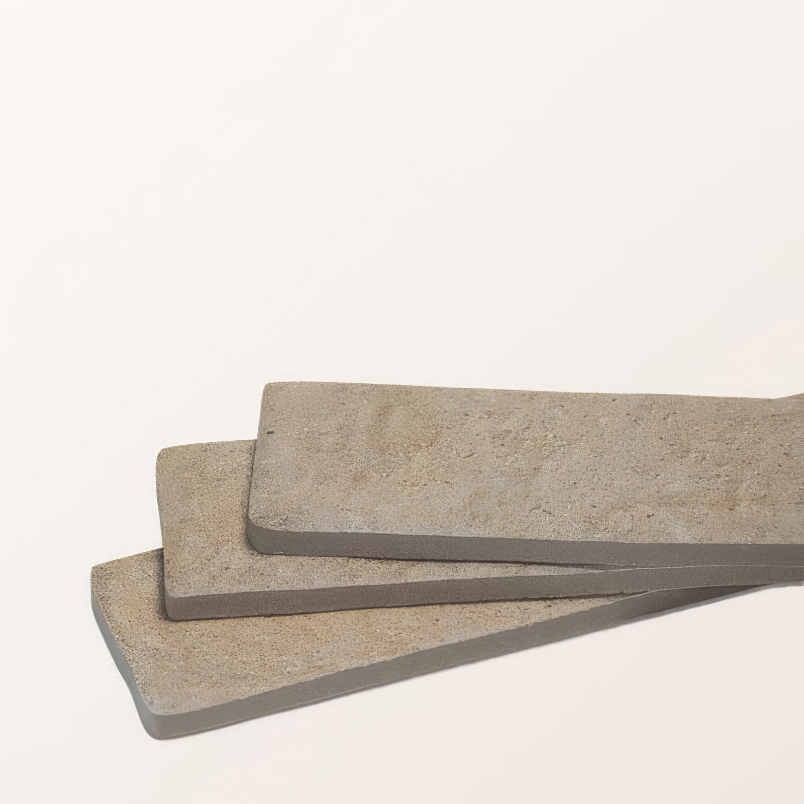 Three stacked buscot porcelain parquet textured concrete tiles with grayish beige textured surface and rounded edges