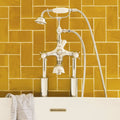 Chrome finished vintage style bathtub faucet with white ceramic handle and showerhead on carnival oro yellow tile wall