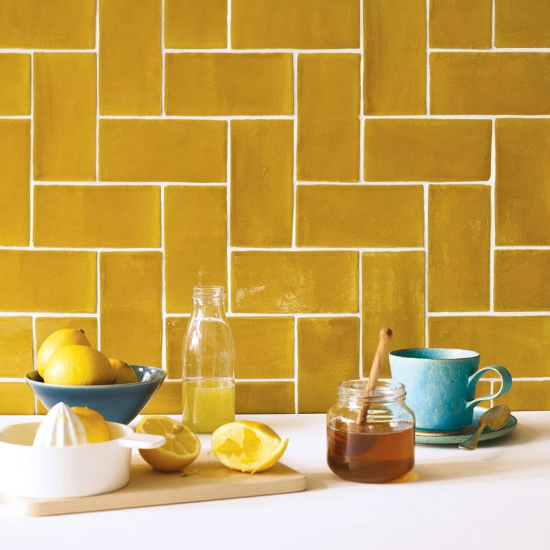 Yellow glazed ceramic tiles with white grout arranged in a herringbone pattern carnival oro yellow tile