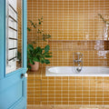 A white bathtub with a chrome faucet set against mustard yellow glossy carnival oro yellow glazed ceramic tiles