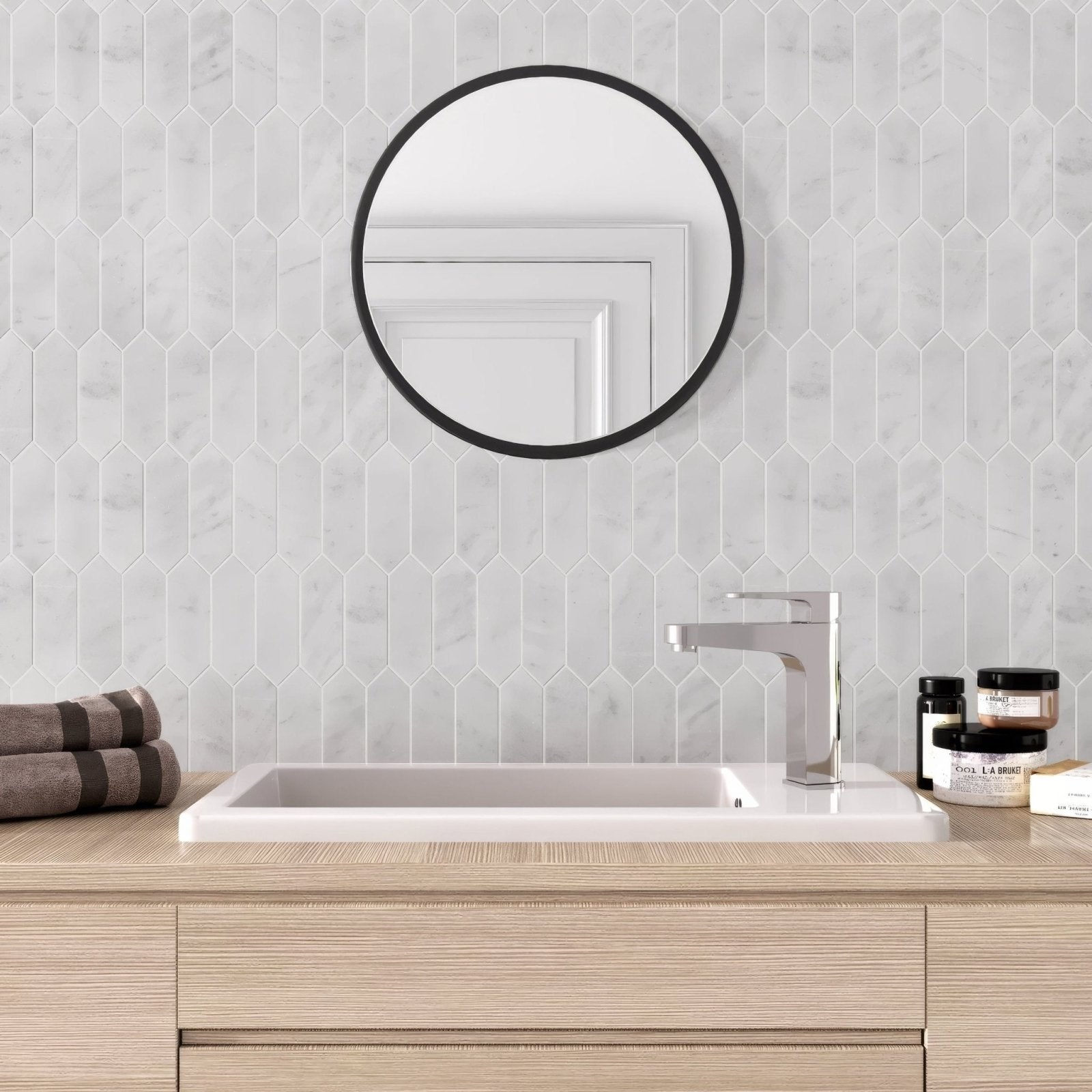 Round black-framed mirror displayed on carrara white marble picket mosaic tile highlighting elegant bathroom decor