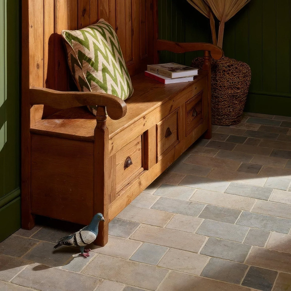 A rustic wooden bench with a green and white zigzag pillow complements castilan limestone cobbles tumbled flooring