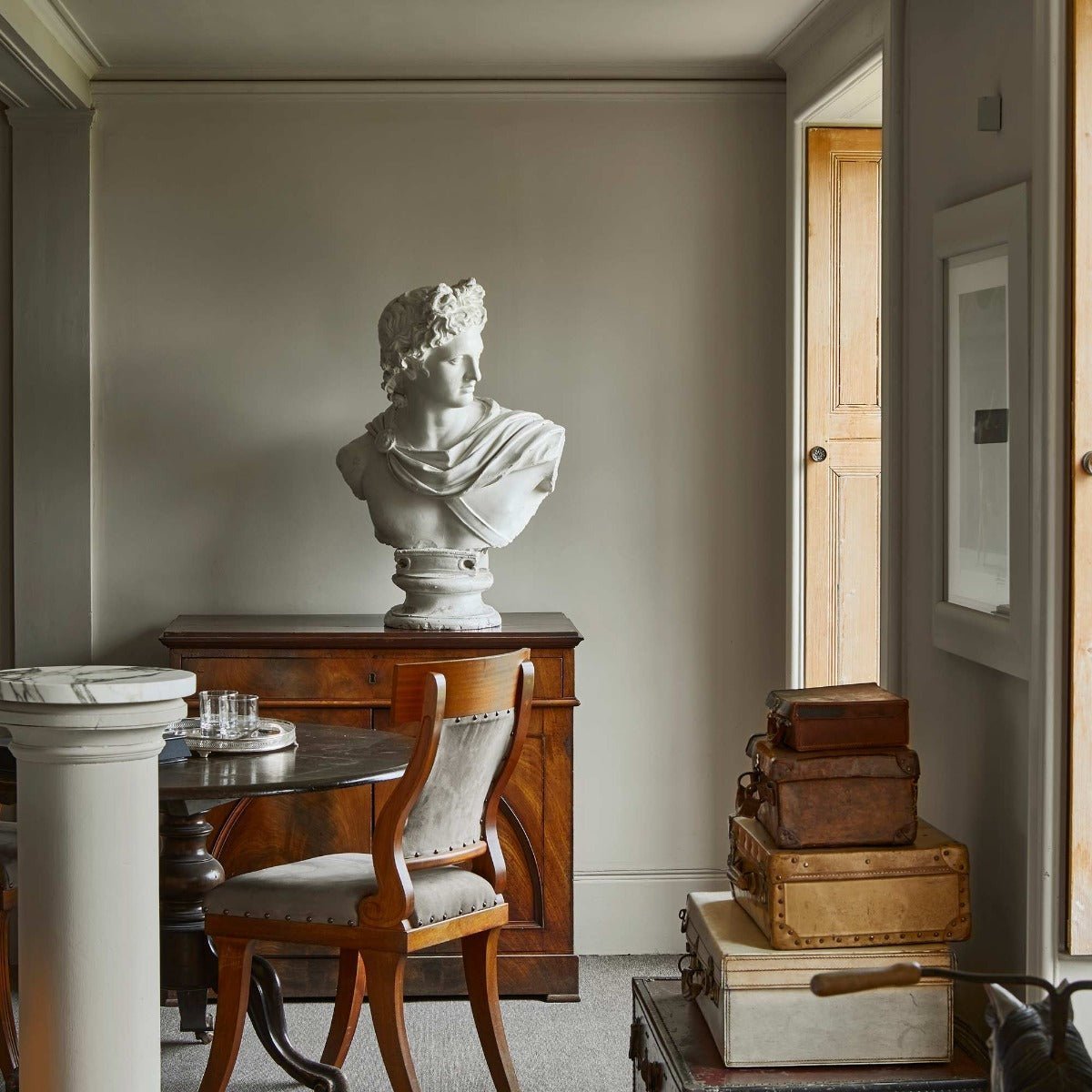 A classical white marble bust with detailed curly hair and draped fabric resting on a pedestal for Celadons robe