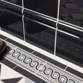Charcoal Grey skirting tile with a gloss ceramic surface, white grout and a scroll-patterned border running above a geometric hall floor