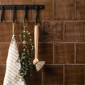 A chestnut field tile with a light wood-handled natural bristle brush hanging from a black metal hook