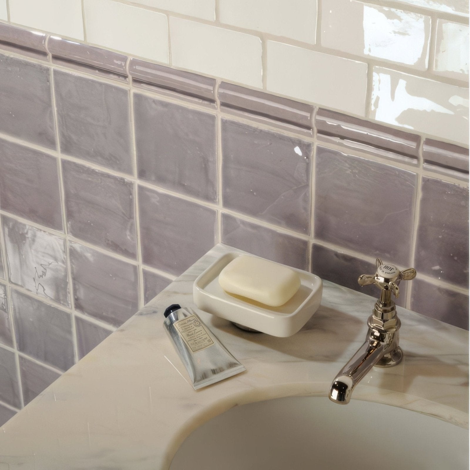 A creamy white bar of soap on a minimalist ceramic dish on a marble countertop featuring china white half tile wall tiles