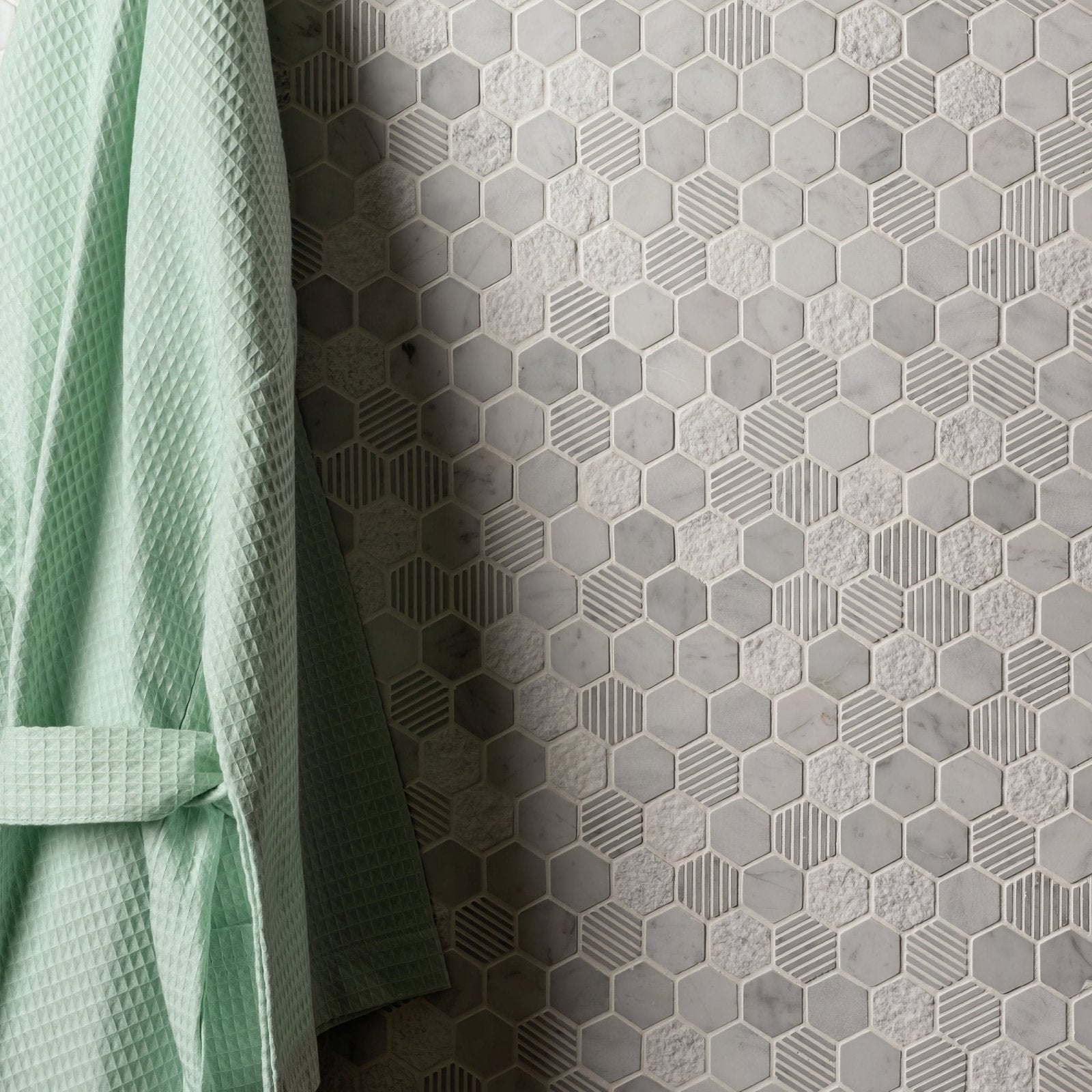 Light green waffle-weave bathrobe hanging beside a wall of gray Cirrus small stone hexagon marble mosaic tiles