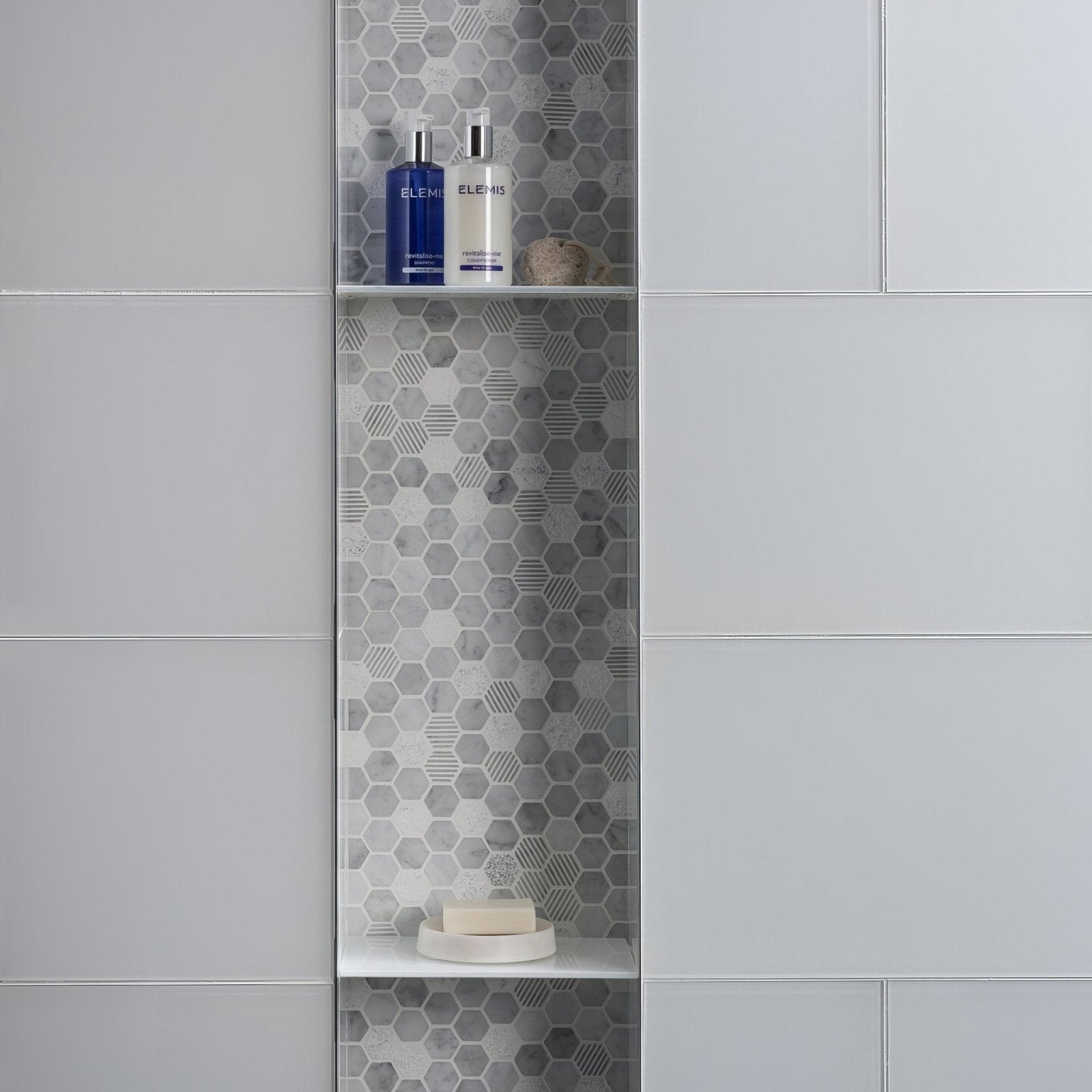 A sleek modern bathroom shelf with white shelves and a hexagonal stone mosaic tile backing for toiletries