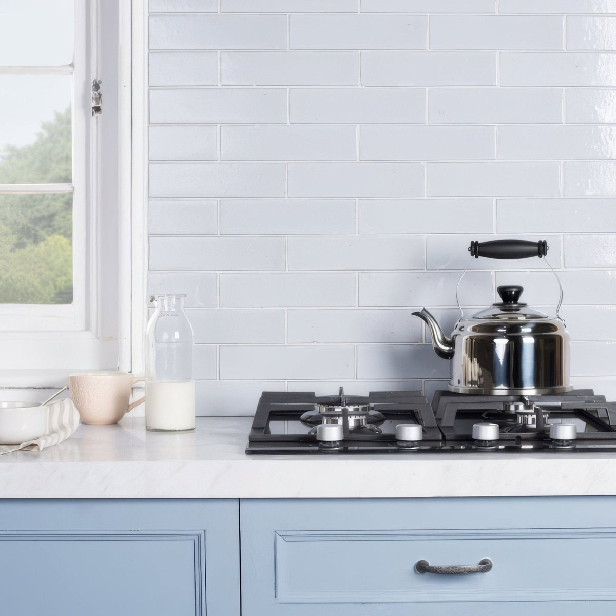 Shiny stainless steel kettle with black handle and lid on gas stove showcasing cloud smooth brick tile background