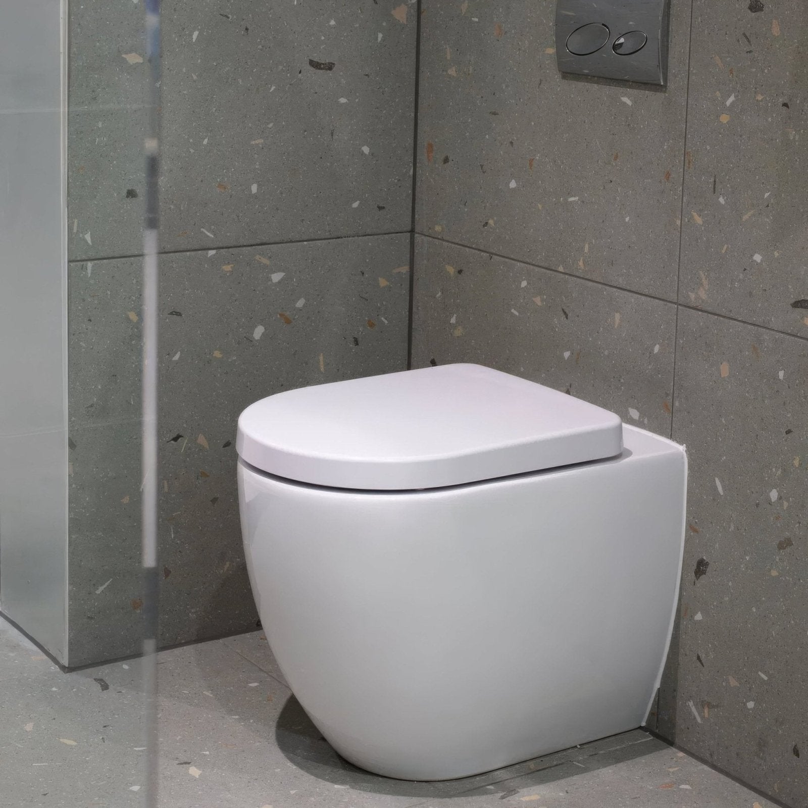 Modern white ceramic toilet with sleek rounded design and matching lid on confetti blue terrazzo effect tile floor