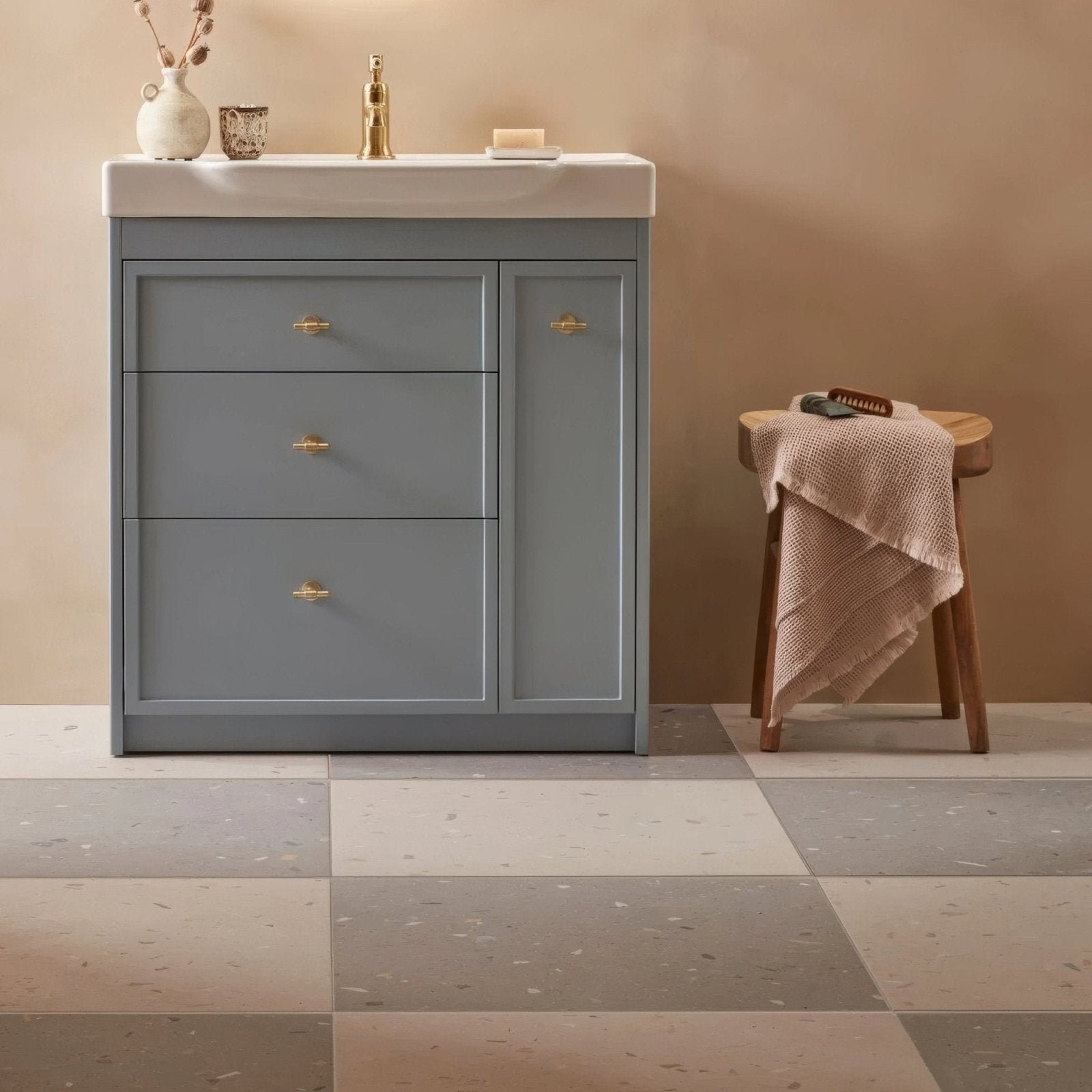 Gray vanity with three drawers and one cabinet door with gold-toned handles against confetti blue terrazzo effect tile