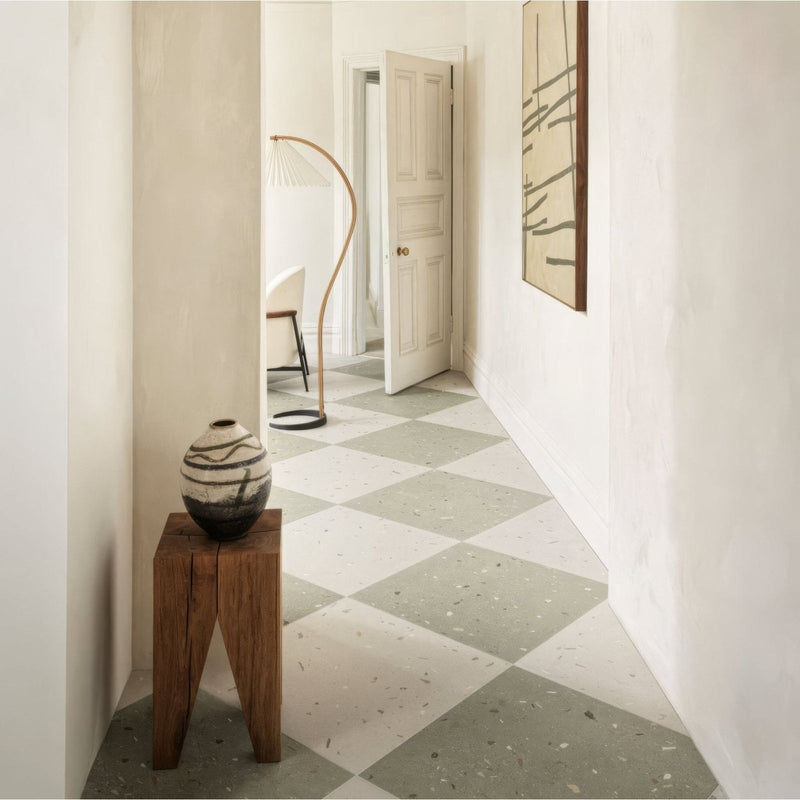 A ceramic vase with black base and white swirling patterns displayed on a rustic wooden pedestal alongside confetti cream terrazzo effect tile