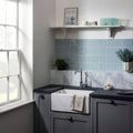 White ceramic farmhouse sink with towel draped over the edge featuring cornflower field tile background