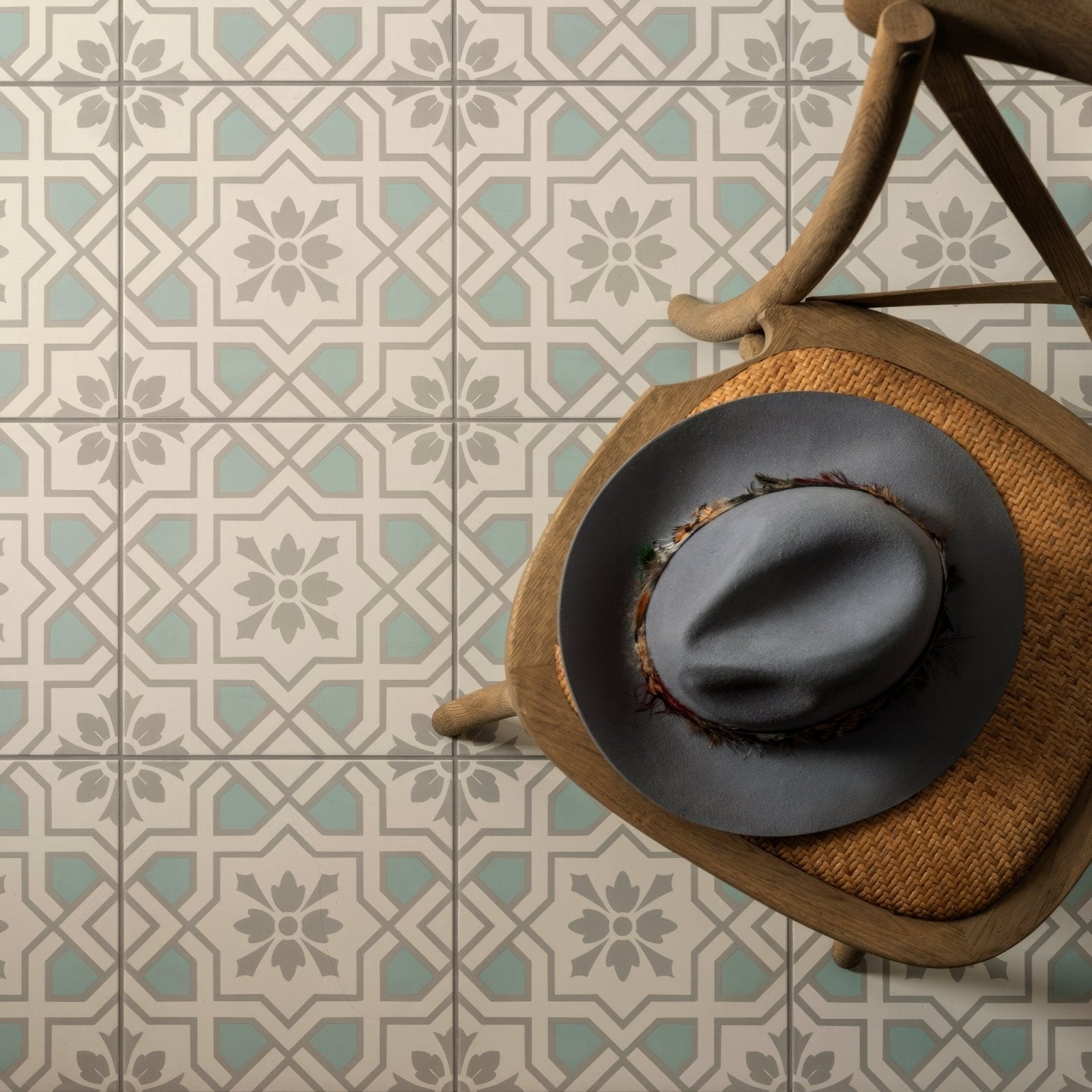 A dark gray felt fedora hat with a decorative feather band resting on a woven wooden chair seat cotehele teal on chalk