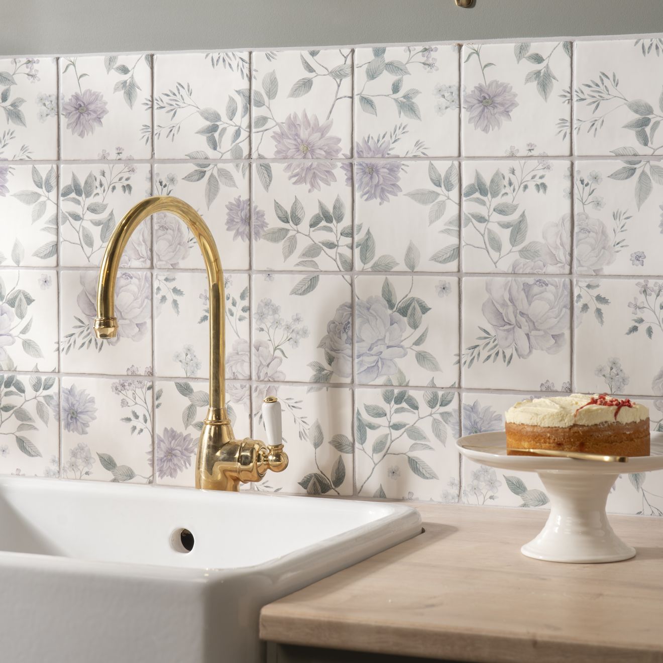 Gold-finished kitchen faucet with curved spout and white ceramic handle above white sink with cottage garden 16 tile panel