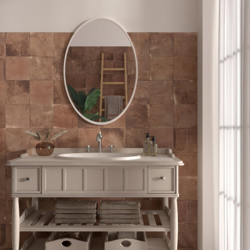 Oval-shaped mirror with white frame mounted above sink featuring cotto cuero terracotta effect tiles background