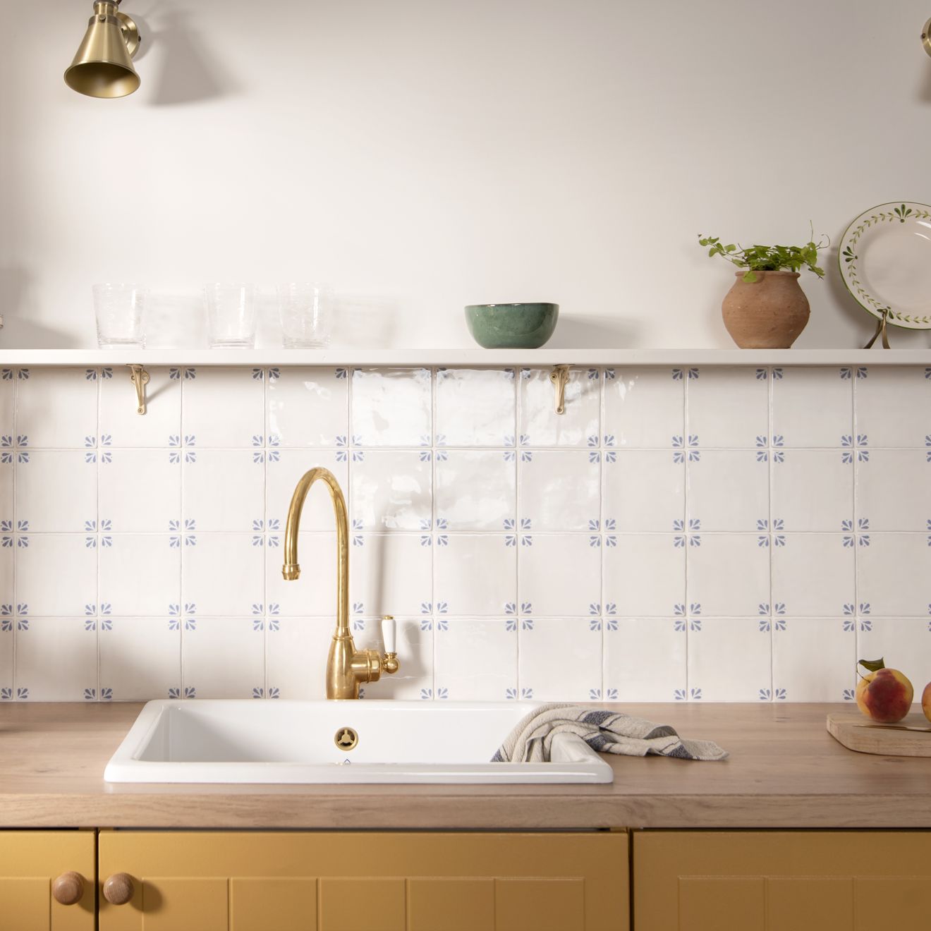 Country Delft Cornelia gold-finished kitchen faucet with curved spout and handle mounted above white ceramic sink
