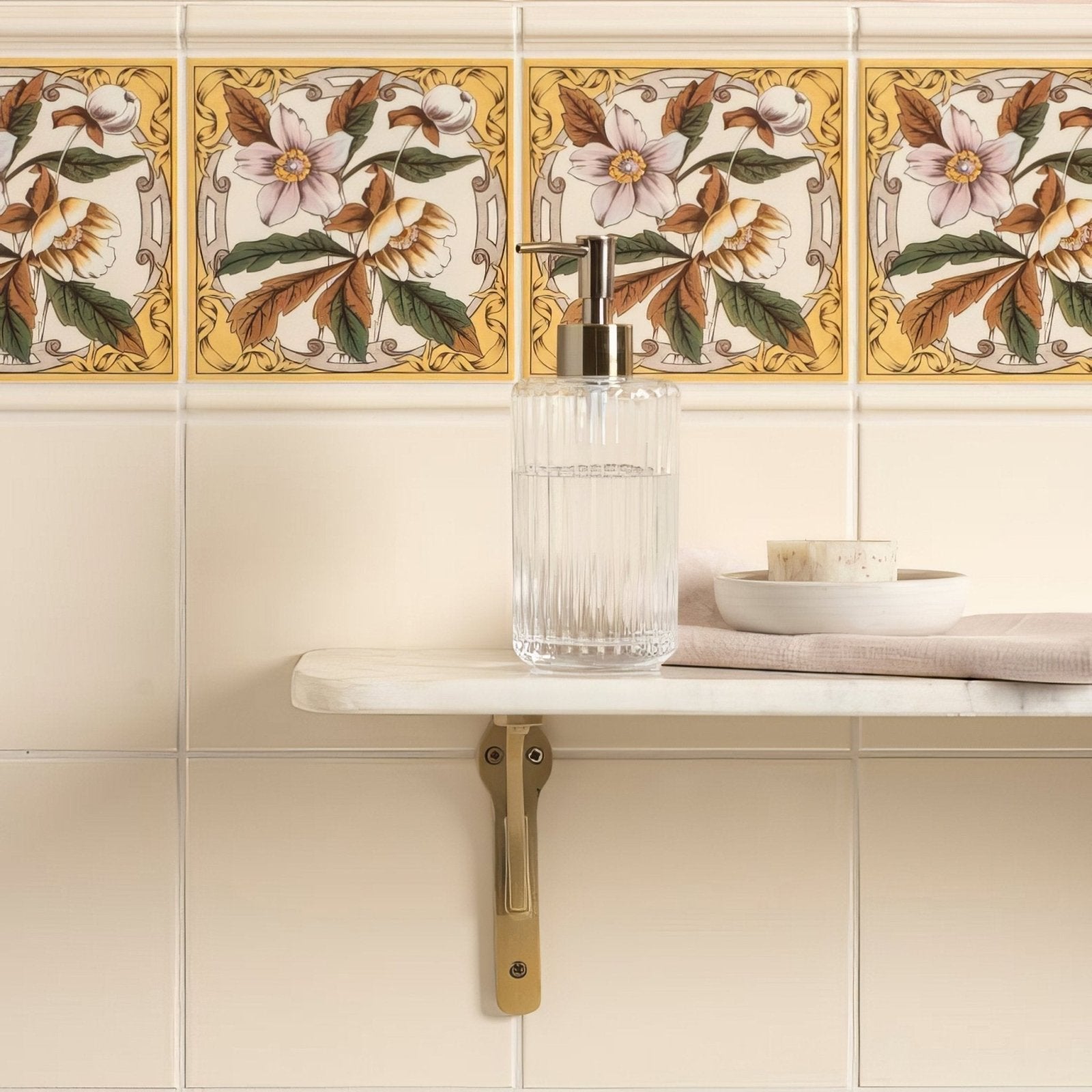 Clear glass soap dispenser with metallic pump displayed on county white field tile surface