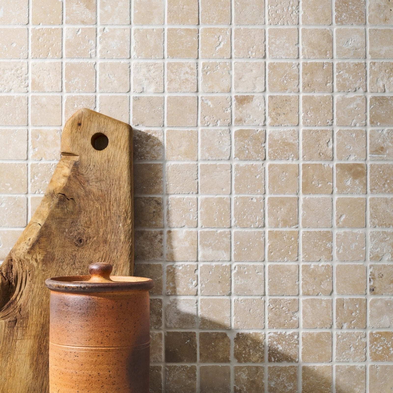 A rustic terracotta ceramic jar with rounded lid and ridges beside a weathered wooden board on crema 4.8 venetian stone mosaic wall